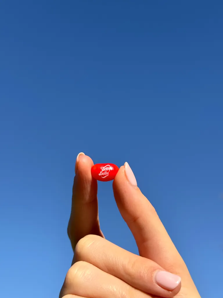 Jelly Belly Very Cherry jelly bean held between fingers — vibrant red color